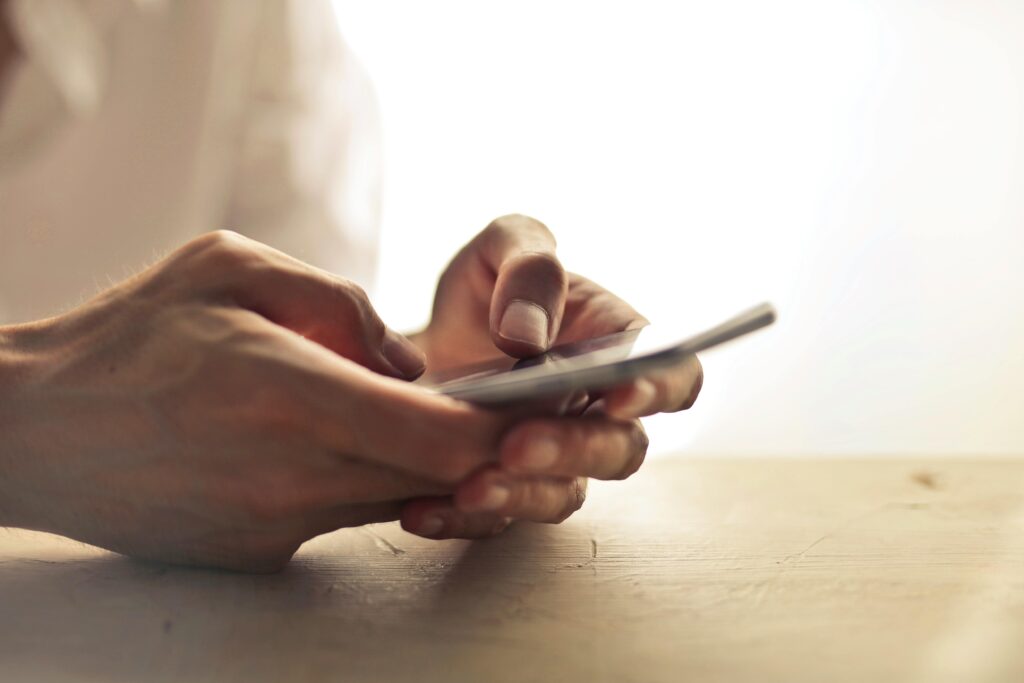 pexels-photo-1458283-1458283 Close-up of an individual's hands holding a smartphone on a table indoors.